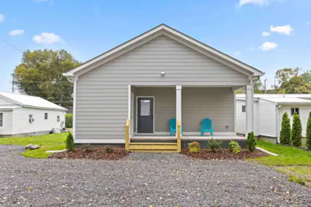 A charming exterior view of the home’s front porch with blue chairs and well-maintained landscaping. The porch is shown as a lively space for socializing or unwinding, with soft lighting that suggests both day and evening use.
