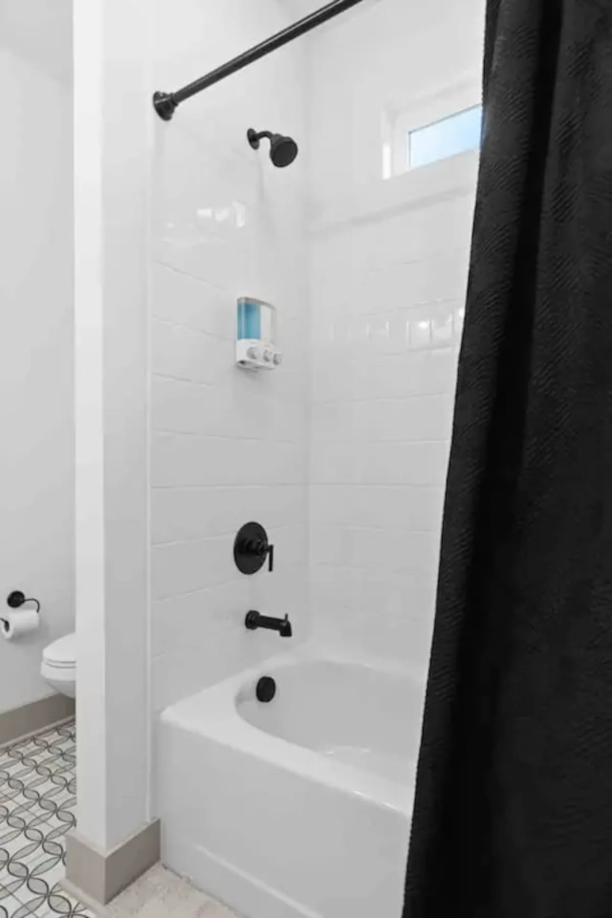 A modern bathroom with a pristine bathtub, stylish decorative tiles, a black shower curtain, and a convenient showerhead. The space feels fresh and inviting, ideal for relaxing soaks or a quick rinse after a busy day.