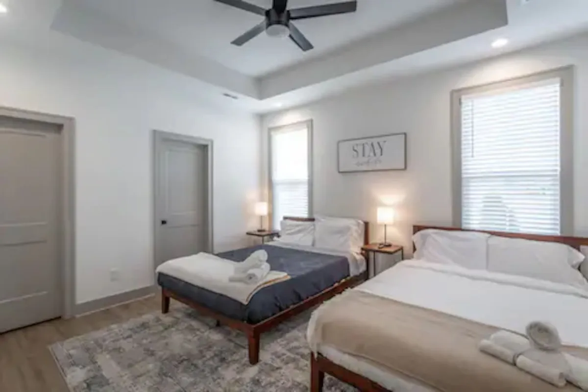 This room contains two beds, each with cozy linens and decorative wall art above, flanked by nightstands with lamps. The layout offers ample space, ideal for families or guests, and conveys a sense of warmth and togetherness.
