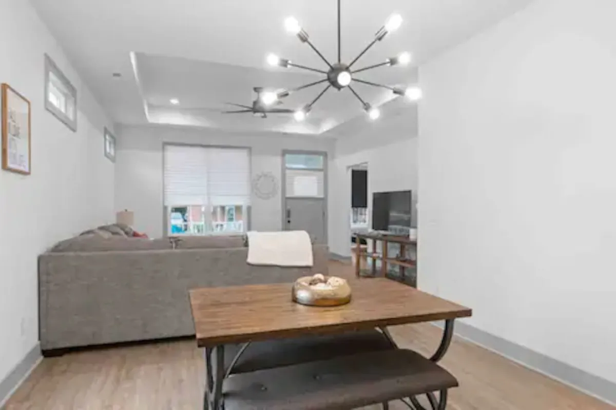A cozy dining area adjacent to a sofa, featuring a modern light fixture and television. The dining table is set in a stylish, inviting space, perfect for family breakfasts, celebratory dinners, or casual coffee conversations.