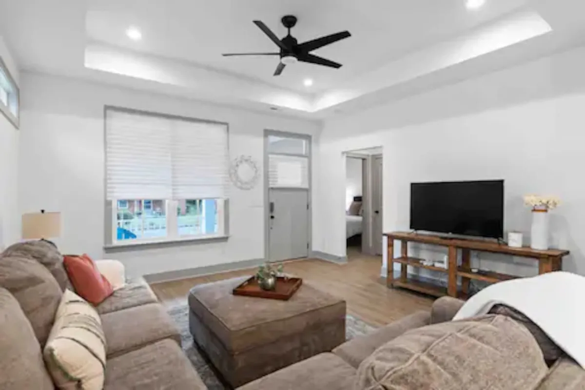This image shows a cozy living area with a sofa, coffee table, TV, window, and door. The space feels bright and welcoming, with natural light streaming in through the window, suggesting an easy transition between indoor comfort and the outside world.