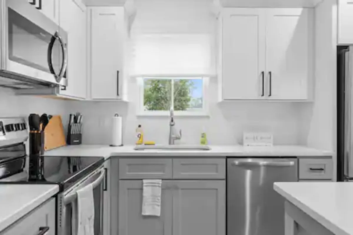 A bright, modern kitchen featuring sleek appliances, a spacious kitchen sink, and a window letting in natural light. The countertops are clutter-free, showcasing elegant finishes and a welcoming cooking space. The view through the window adds an airy, inviting feel to the room.