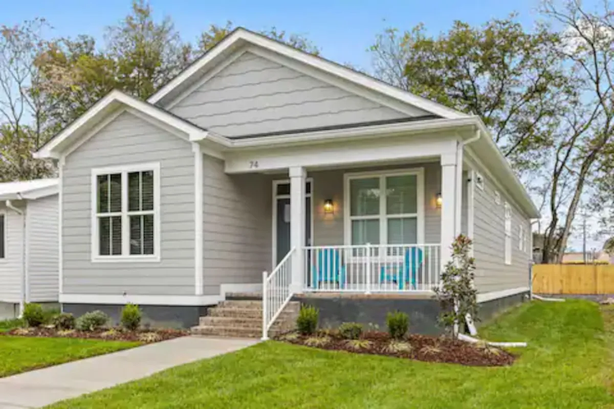 The image showcases the front exterior of a newly constructed single-family home in downtown Chattanooga. A welcoming front porch is adorned with colorful chairs and surrounded by a neatly landscaped garden, evoking a homey and inviting atmosphere. The scene suggests opportunities for relaxing with morning coffee, reading, or gathering with friends, all while taking in city views and seasonal blooms.
