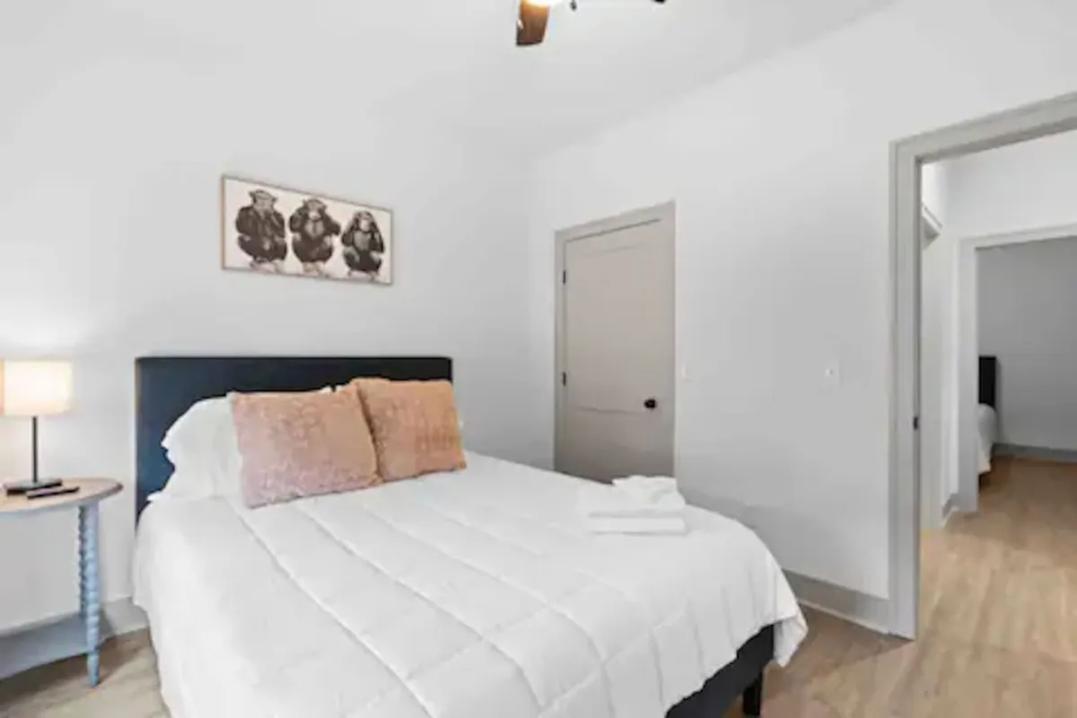 This image features a neatly made bed adorned with decorative pillows, a nightstand with a lamp, and tasteful wall art. The lighting and decor create a cozy, welcoming atmosphere that emphasizes comfort and relaxation—ideal for unwinding after a long day.
