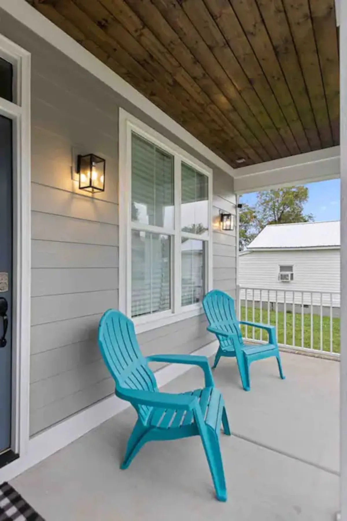 A close-up shot of a cozy porch corner with turquoise chairs, a wooden ceiling above, and glowing outdoor lights. The scene conveys a sense of warmth and relaxation, ideal for enjoying morning coffee or evening breezes.