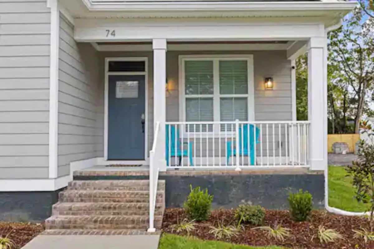 A welcoming front porch featuring blue chairs, brick steps leading up to the door, and tasteful seasonal decorations. The space looks cozy and inviting, bathed in natural light, and hints at both morning coffee moments and evening relaxation.