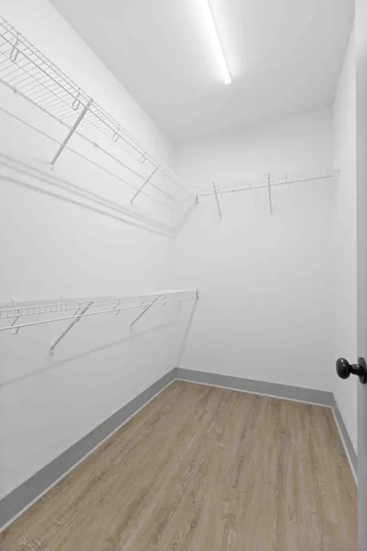 A functional laundry area featuring wire shelving units, smooth walls, and laminate flooring. The space is minimalist and organized, making it easy to sort and refresh clothes during your stay.